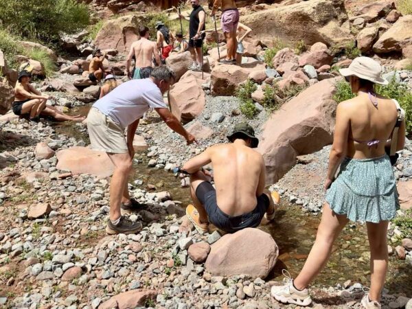 Groupe de randonneurs marchant le long d'un sentier rocailleux des Gorges de l'Oukaïmeden, entourés de paysages montagneux sous un ciel dégagé.